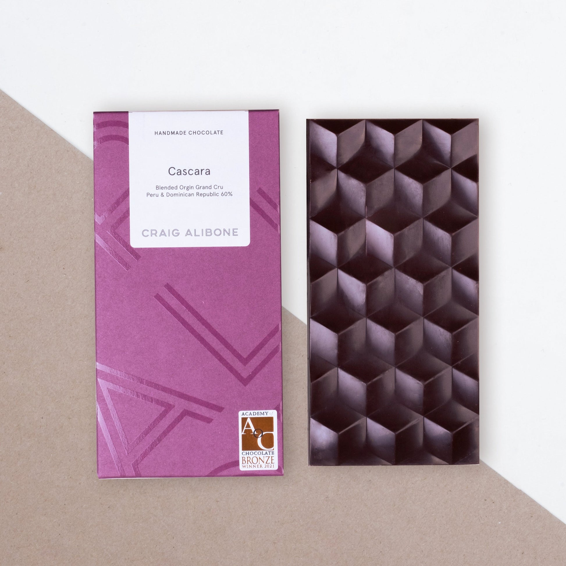 Photo of a chocolate bar packaging sized by side with the unpacked chocolate bar.  You can see the beautifully designed packaging and textured pattern on the chocolate bar. 